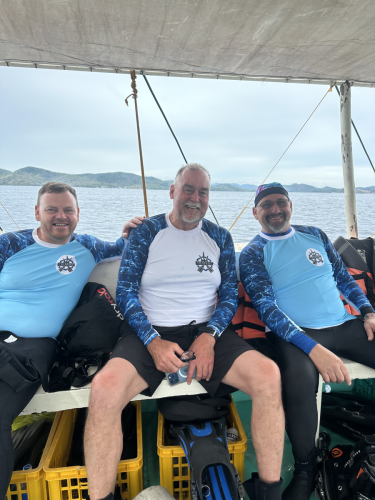 A few scuba divers in their Trident Warriors shirts taking a group picture while on the boat in the Philippines during the 2025 trip